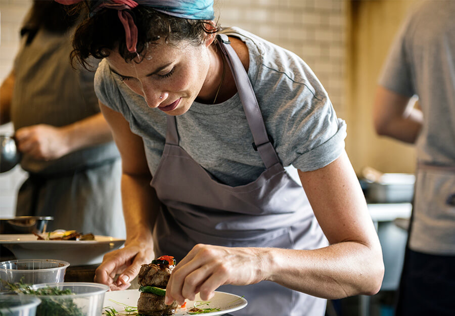 Chef in a grey apron carefully plating a dish in a professional kitchen.