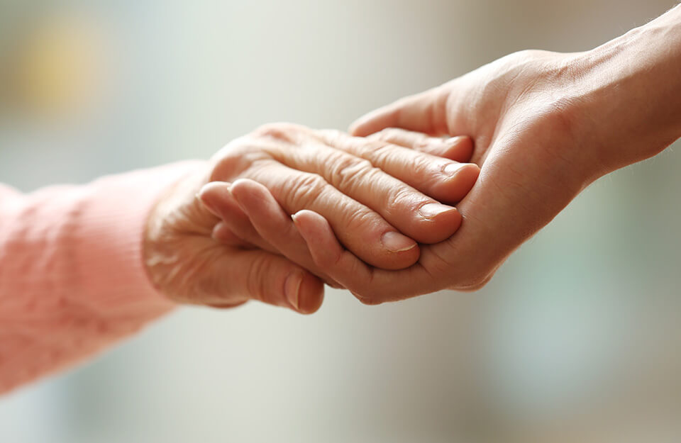 Close-up of a younger hand holding an older hand, symbolizing care and support.