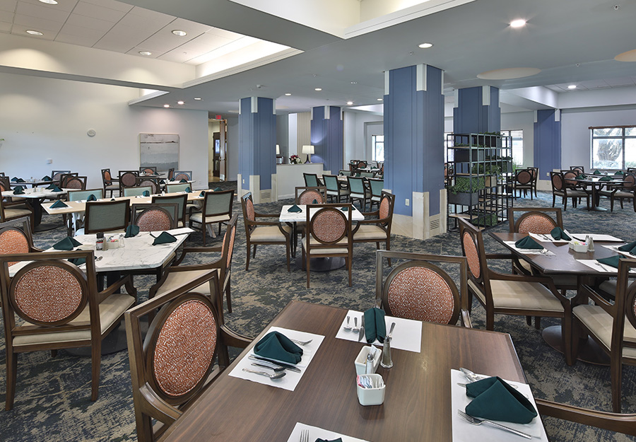 Spacious dining area with neatly set tables and chairs in a senior living community.