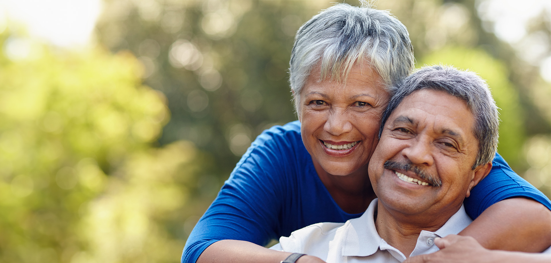 Smiling senior couple hugging outdoors in a sunny garden, enjoying their time together.