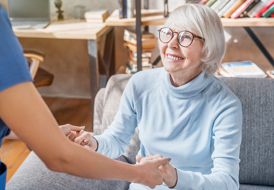 Smiling senior woman holding hands with caregiver in a cozy living space.