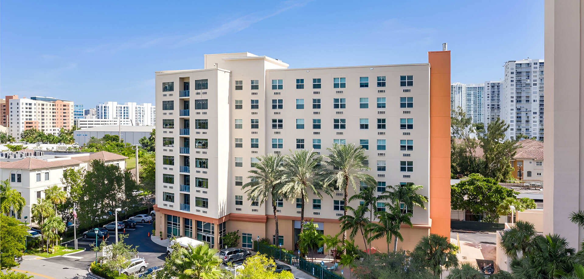 Exterior view of a modern, multi-story senior living facility surrounded by greenery and palm trees.