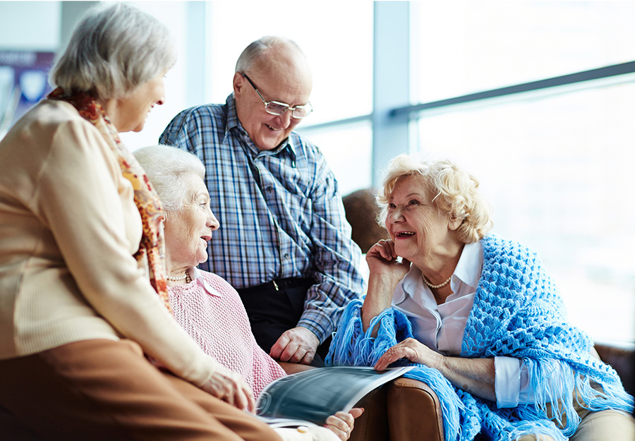 Group of seniors smiling and chatting in a bright common area of a senior living community.