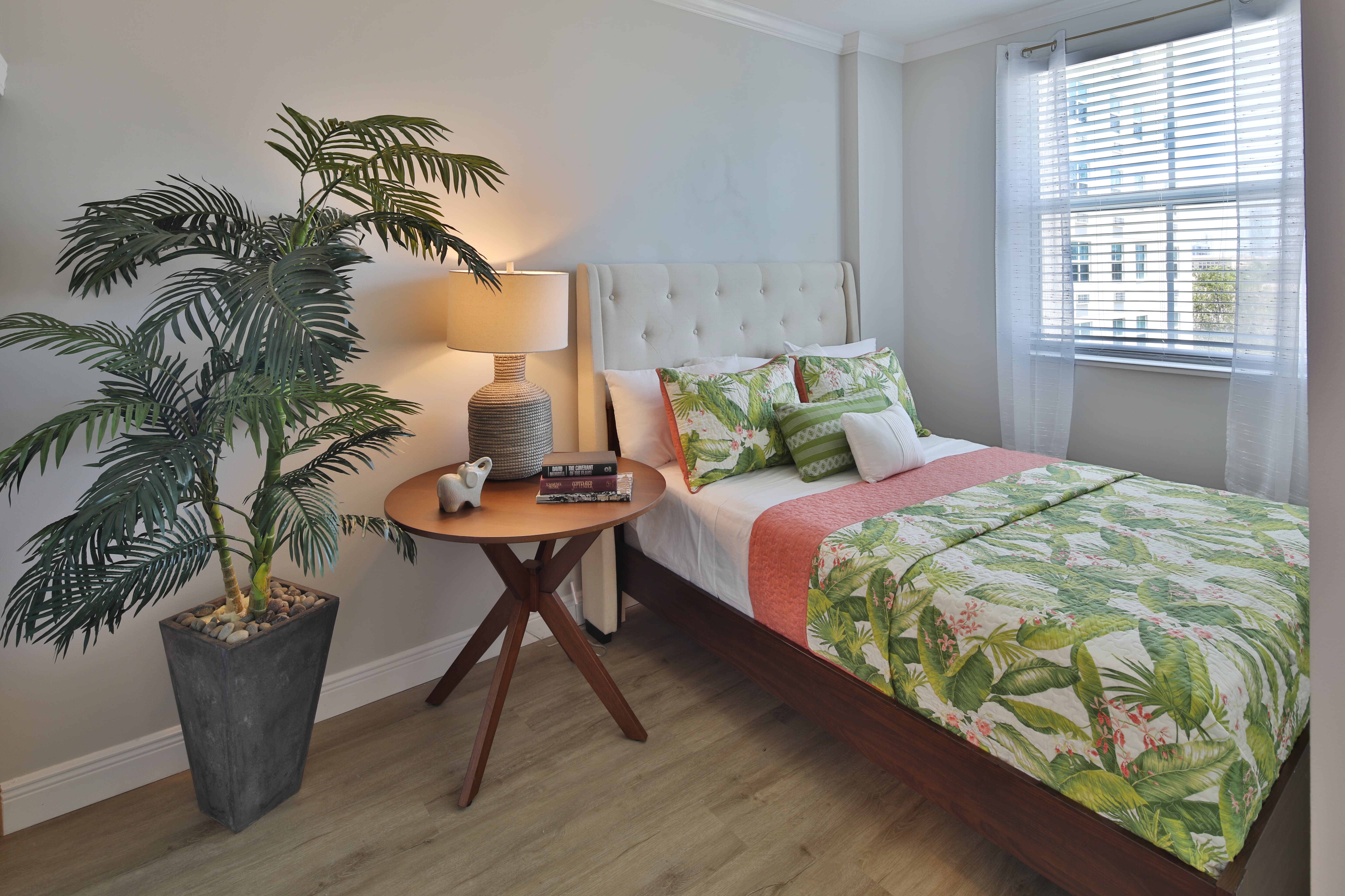 Tropical-Themed Bedroom with Vibrant Decor Tropical-themed bedroom with large plant, bed with green and orange decor, and a side table.