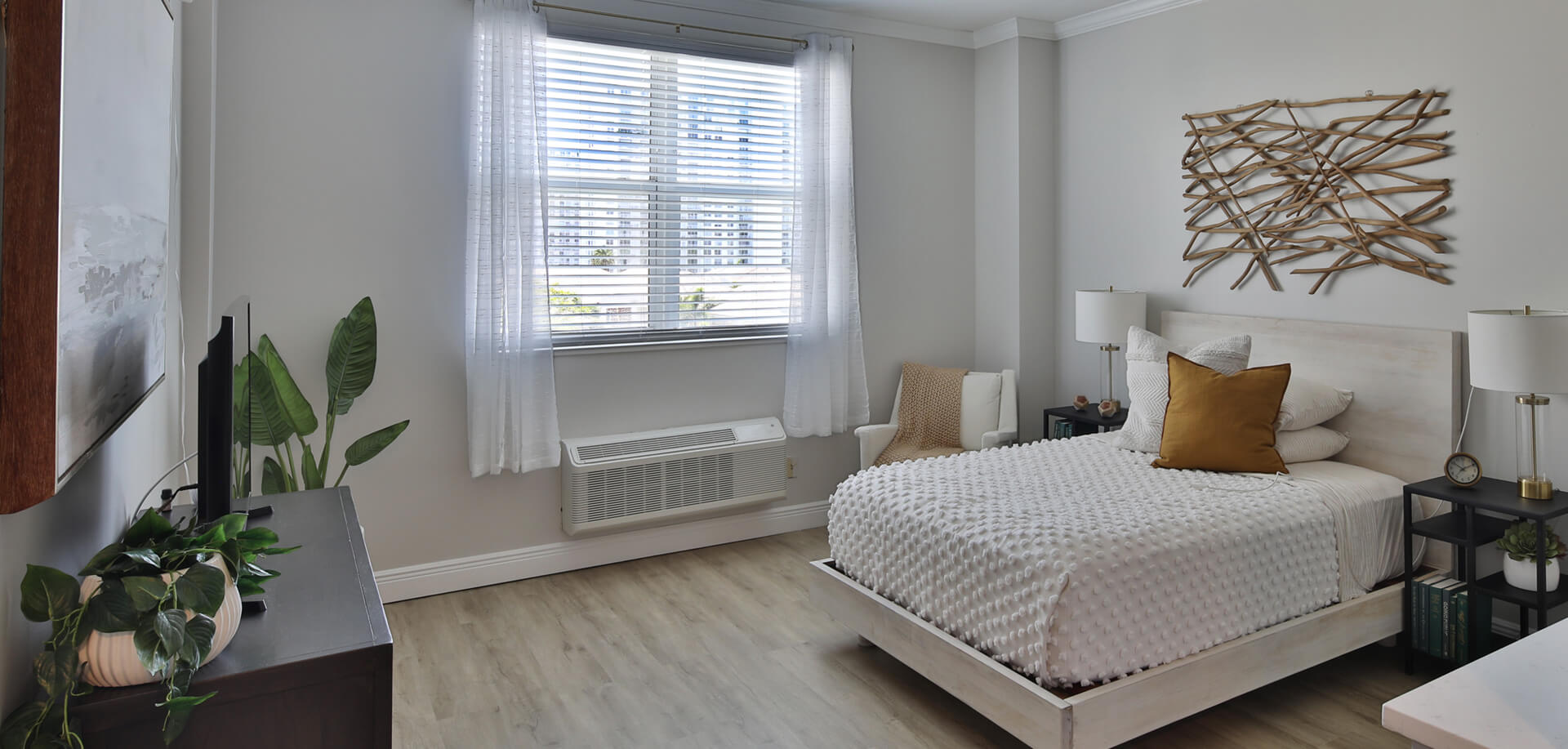 Bright, modern studio unit interior with bed, plants, wall art, and a window with city view.